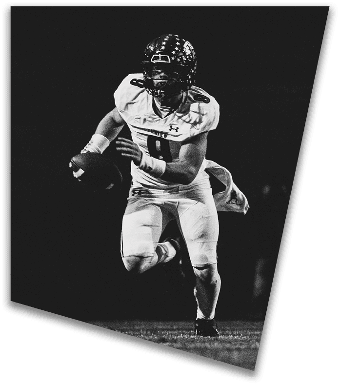 A person wearing a dark football uniform and helmet with “American Canyon" on the jersey is kneeling on one knee on a field at night. Description generated by AI