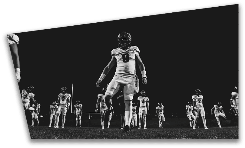People wearing black American Canyon football uniforms and helmets are standing on a football field at night. Description generated by AI