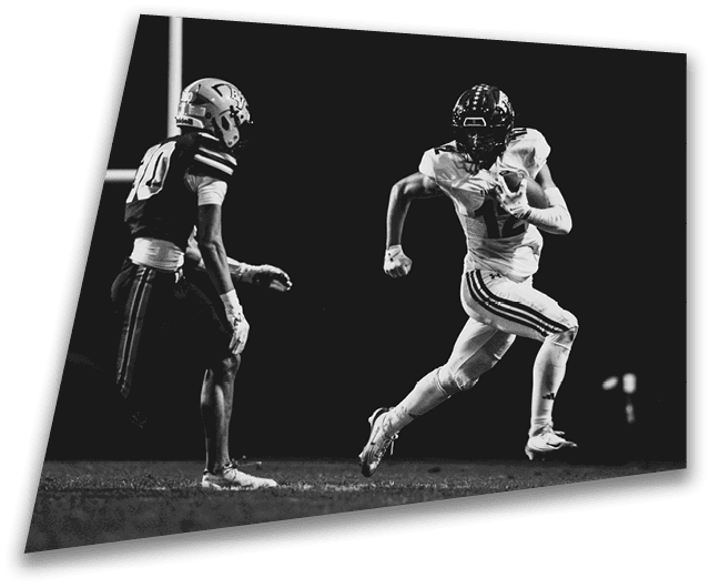 Four people in dark football uniforms and helmets stand in a row on a field, appearing focused and ready for action. Description generated by AI
