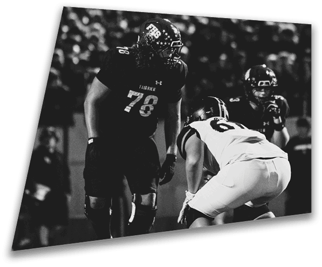 Four people in dark football uniforms and helmets stand in a row on a field, appearing focused and ready for action. Description generated by AI
