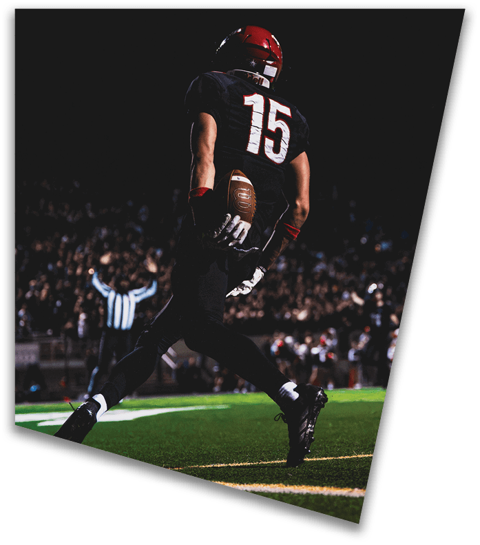 A person wearing a dark football uniform and helmet with “American Canyon" on the jersey is kneeling on one knee on a field at night. Description generated by AI
