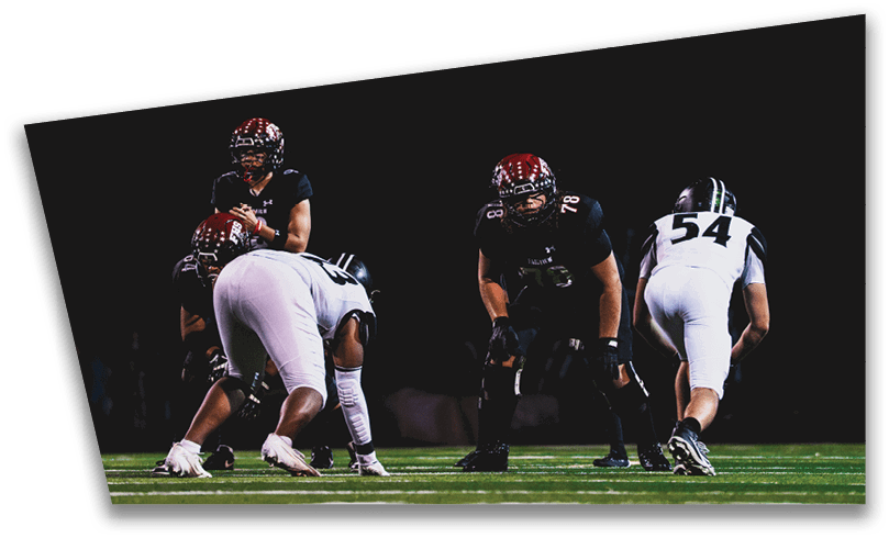 People wearing black American Canyon football uniforms and helmets are standing on a football field at night. Description generated by AI