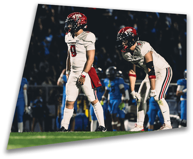 Four people in dark football uniforms and helmets stand in a row on a field, appearing focused and ready for action. Description generated by AI