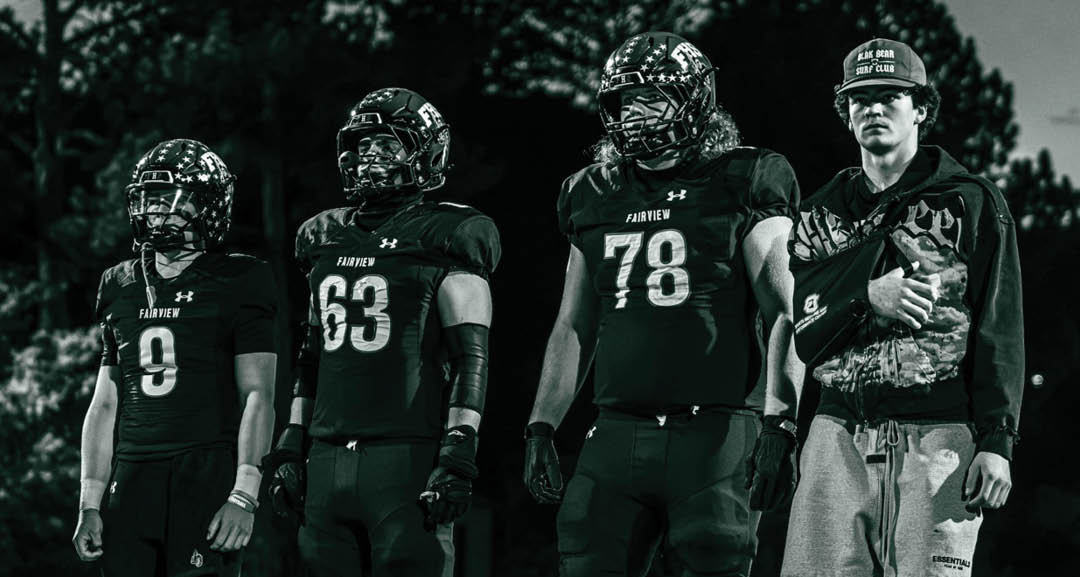 Four people wearing black football uniforms with “VISTA" on the front are standing together in a stadium with a crowd in the background, two of them holding helmets raised above their heads. Description generated by AI