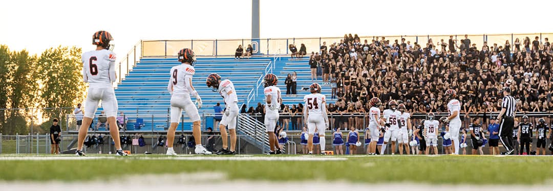 Four people wearing black sports jerseys with “VISTA" on them stand closely together in front of a large crowd, with one person raising an arm in celebration. Description generated by AI
