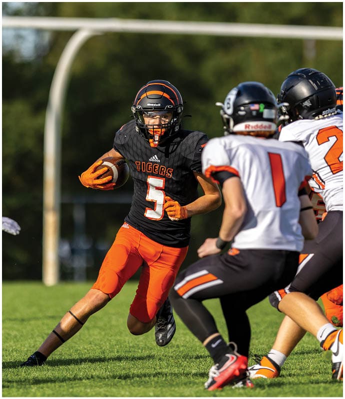 Three football players in blue and white uniforms running on a field. Description generated by AI