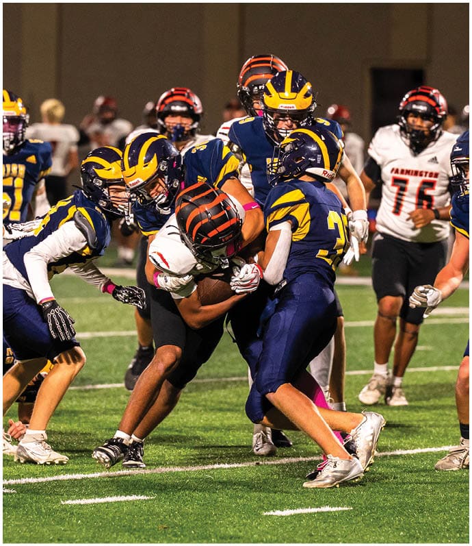 Three football players in blue and white uniforms running on a field. Description generated by AI
