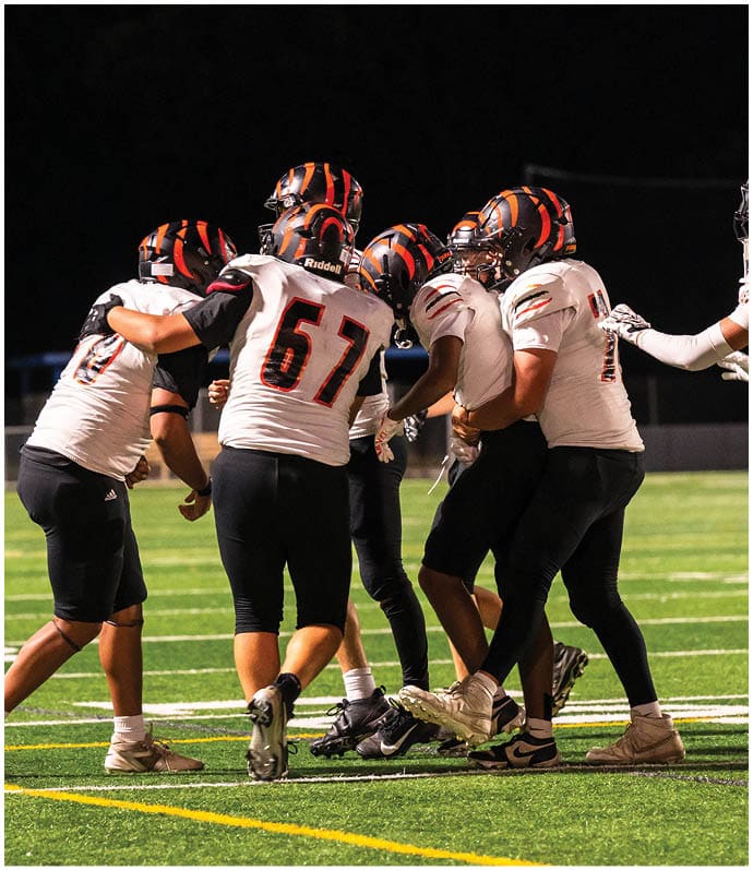 Three football players in blue and white uniforms running on a field. Description generated by AI