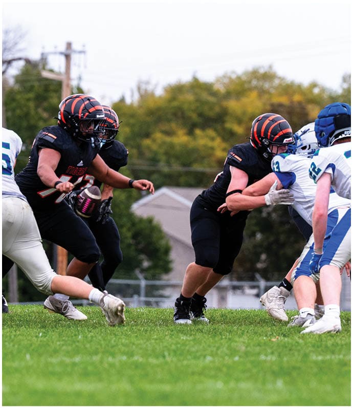 Three football players in blue and white uniforms running on a field. Description generated by AI