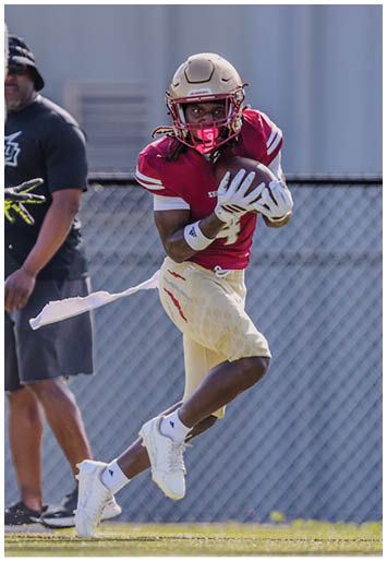 Two people in football uniforms are actively playing on a field with one person running while holding the ball and the other person chasing. Description generated by AI