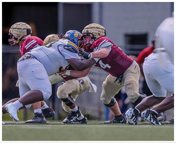 People wearing helmets and protective gear are engaged in a football game on a grassy field. Description generated by AI