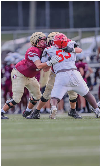 Two people in maroon and gold football uniforms are blocking a person in a white and red football uniform during a game on a grassy field. Description generated by AI