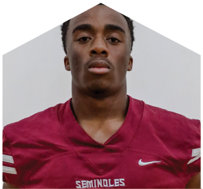A person wearing a maroon football jersey with the word Seminoles and a Nike logo stands facing forward against a plain background. Description generated by AI