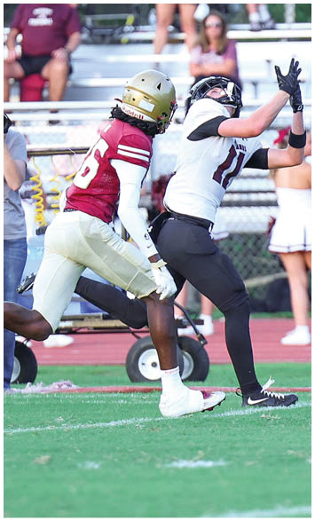 A football player is throwing a ball on a field while cheerleaders and spectators watch from the bleachers in the background. Description generated by AI