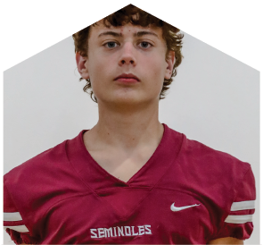 A person with curly hair wearing a maroon football jersey with the word “SEMINOLES" and a Nike logo stands against a plain background. Description generated by AI