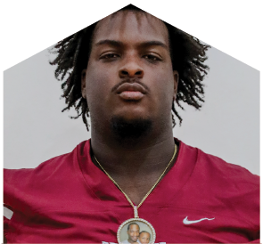 Person with tousled hair wearing a maroon sports jersey with the word “SEMINOLES" on the front. Description generated by AI