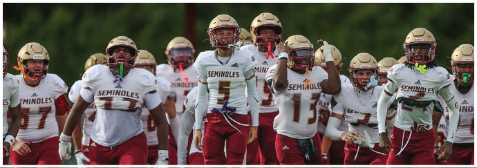 A group of people wearing football uniforms with helmets and pads are walking together on a field. Description generated by AI
