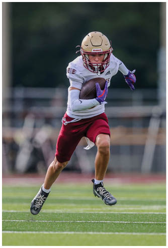 A person wearing a football helmet and uniform is running on a field while holding a football securely. Description generated by AI
