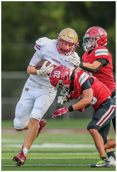 Two people in football uniforms are engaged in a tackle on a green field during a game. Description generated by AI