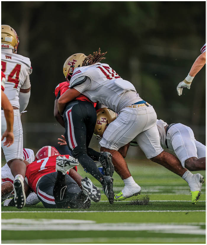 Two people in football uniforms are engaged in a tackle on a grassy field during a game. Description generated by AI