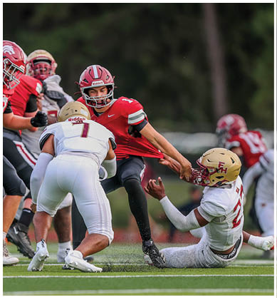 Two people in football uniforms are engaged in a play with one pulling the other's jersey while other players are visible in the background. Description generated by AI