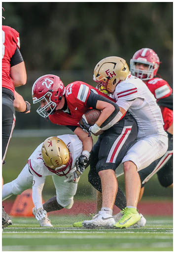 A group of people in football uniforms are engaged in a tackle on a grassy field during a game. Description generated by AI