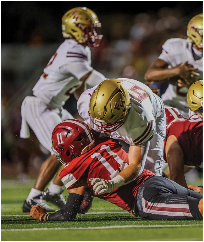 Several football players in helmets and uniforms are engaged in a close, intense play on the field during a game. Description generated by AI