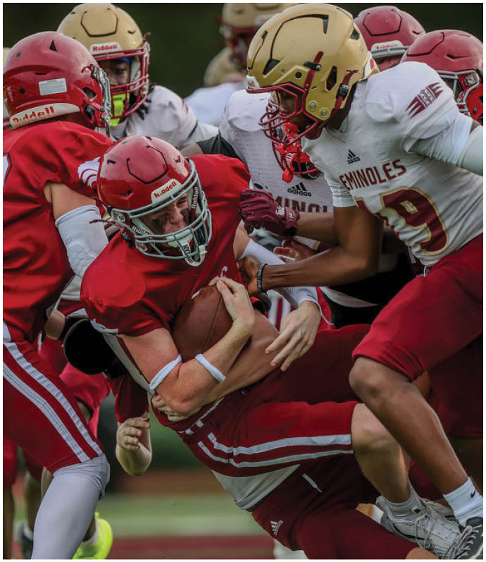 Several people in football uniforms are engaged in a tackle during a game on a field. Description generated by AI