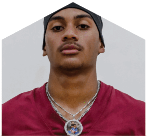 Person wearing a maroon sports jersey and a black head covering with two silver chains around their neck, one featuring a round pendant with a small photo inside. Description generated by AI