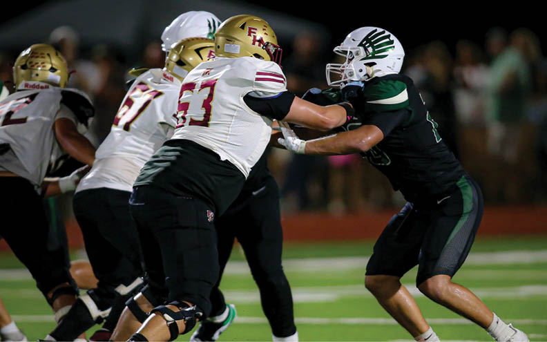 Two people in football uniforms are engaged in a physical play on a field with one person pushing against the other's chest. Description generated by AI