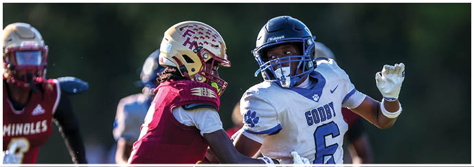 Two people in football uniforms are engaged in a play on a field with one person wearing a white jersey and the other wearing a maroon jersey. Description generated by AI