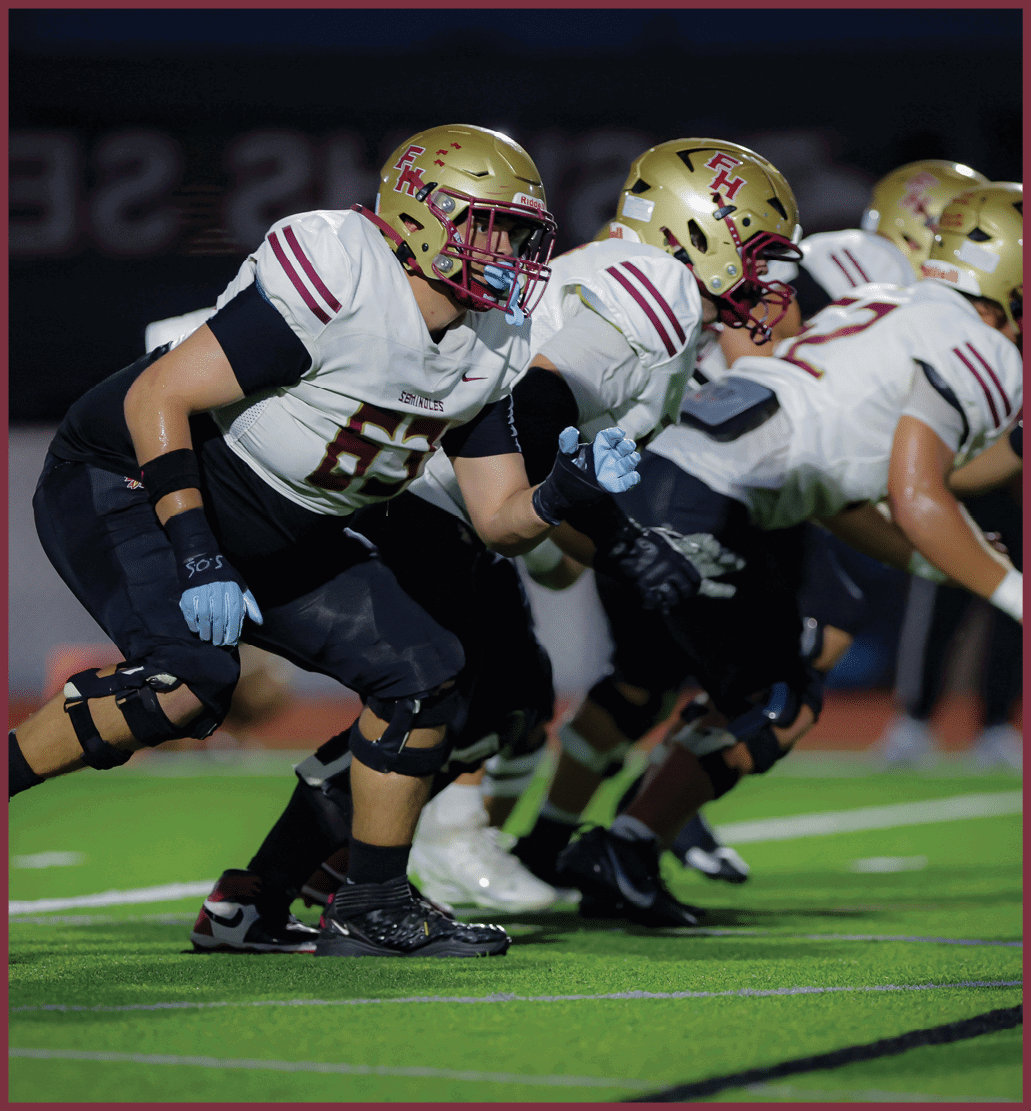Several people in football uniforms and helmets are lined up in a ready stance on a field, preparing for a play. Description generated by AI