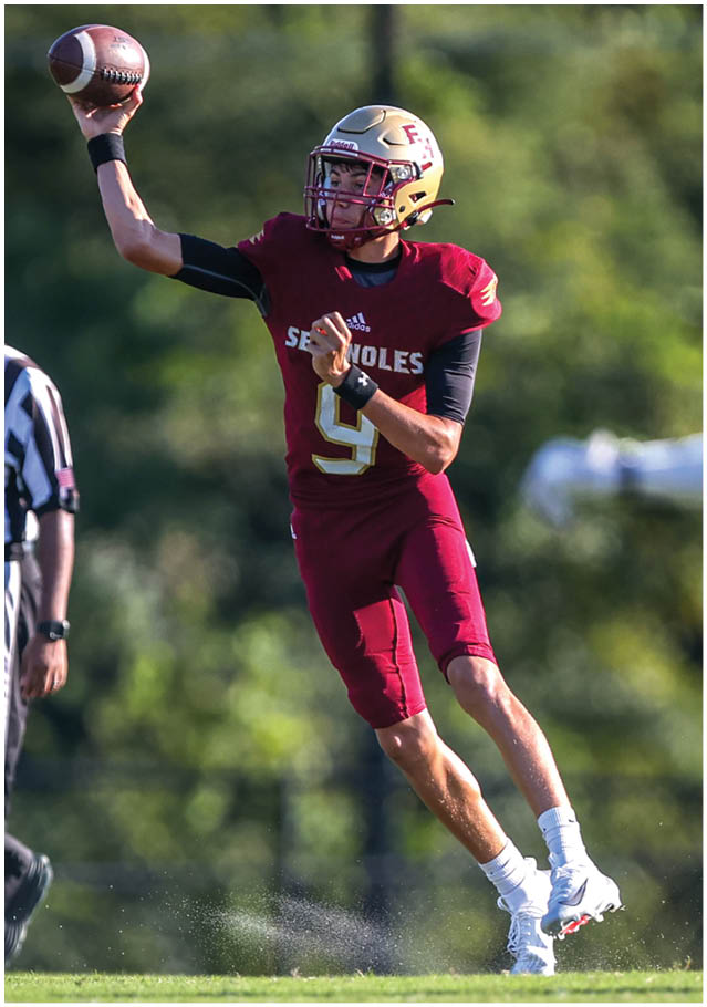 A person wearing a maroon football uniform with the number nine is throwing a football on a grassy field while a referee and another player in white are nearby. Description generated by AI