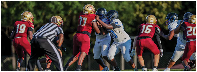 Adults wearing football uniforms are engaged in a game on a grassy field with trees in the background. Description generated by AI