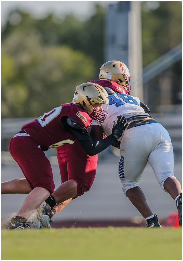 Two people in football uniforms are engaged in a tackle on a grassy field during a game. Description generated by AI