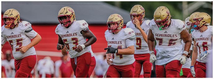 Adults wearing football uniforms with “Seminoles" on their jerseys are running on a field during a game or practice. Description generated by AI
