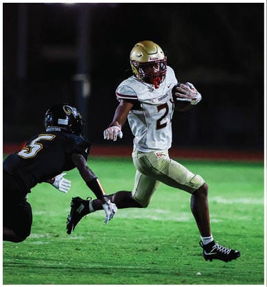 A person wearing a gold football helmet is visible at the bottom of the image against a dark background with partially visible illuminated numbers and letters on the left side. Description generated by AI