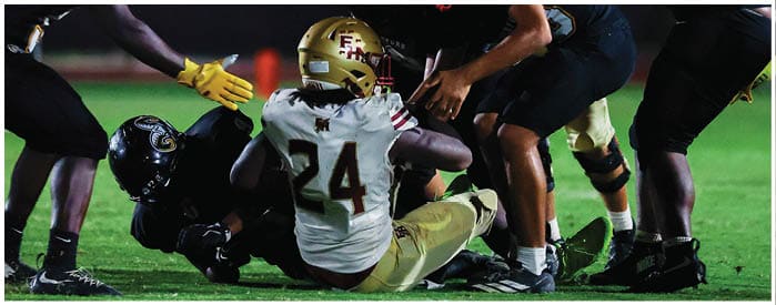 Two football players in helmets and uniforms are positioned on a field under stadium lights during a game. Description generated by AI