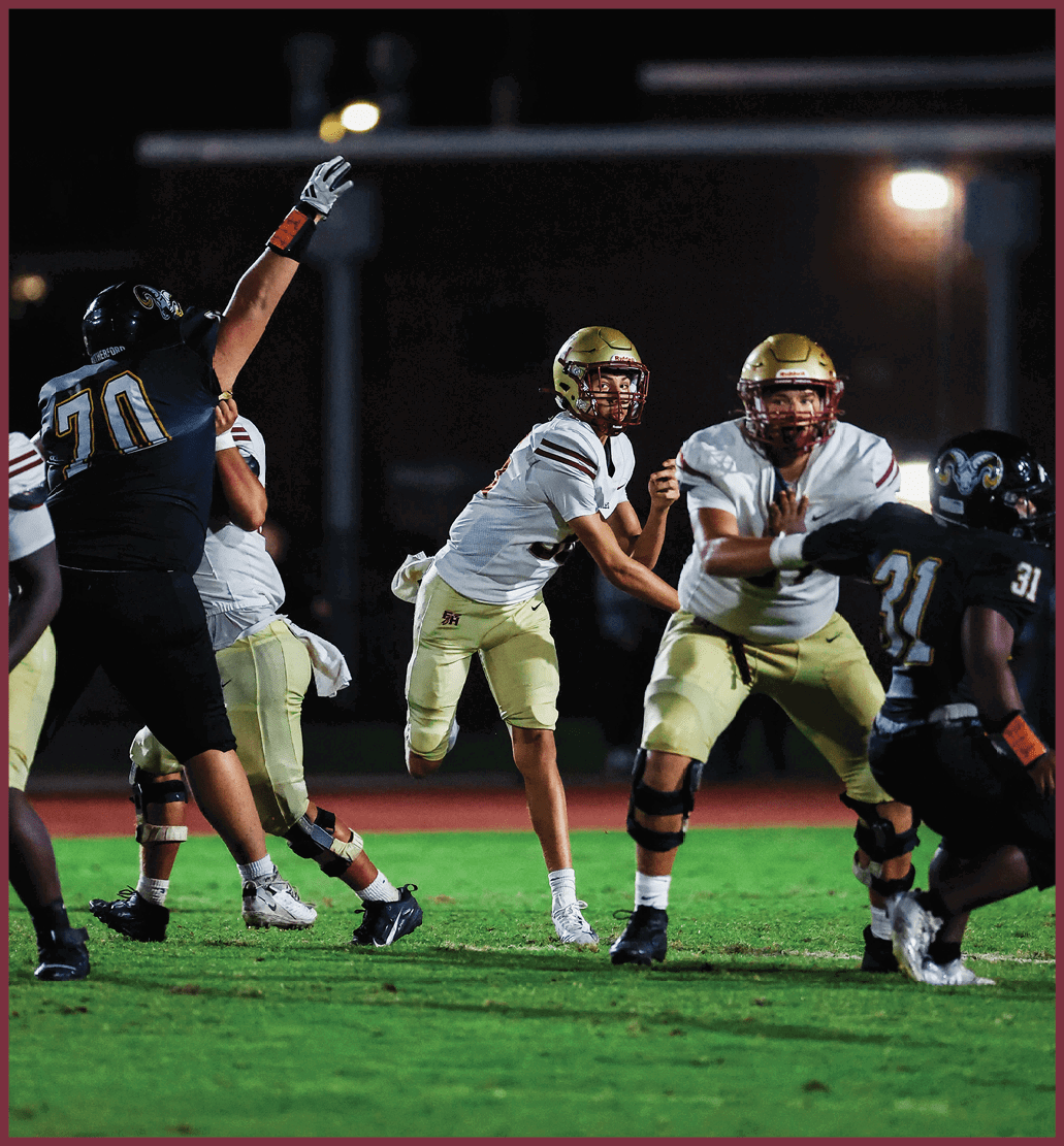 A person wearing a glove raises an arm while two people in football helmets and uniforms look ahead during a nighttime outdoor event. Description generated by AI