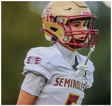 A person wearing a football helmet and a white jersey with “SEMINOLES" written on it is looking to the side. Description generated by AI