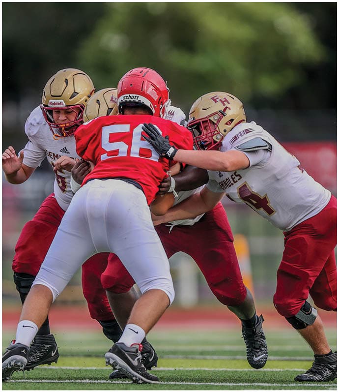 Four people in football uniforms are engaged in a play on a field with three wearing white and red uniforms and one wearing a red and white uniform. Description generated by AI