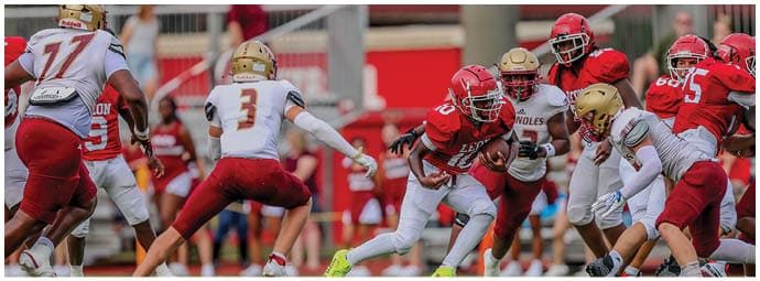 People wearing red and white football uniforms are actively engaged in a play on a football field. Description generated by AI