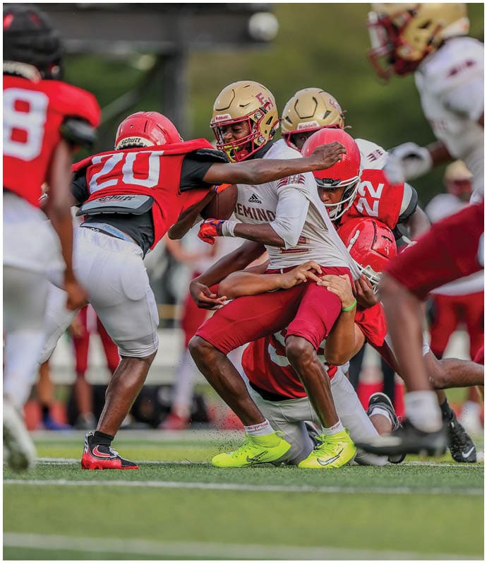 Several people wearing football uniforms are engaged in a tackle on a grassy field during a game. Description generated by AI