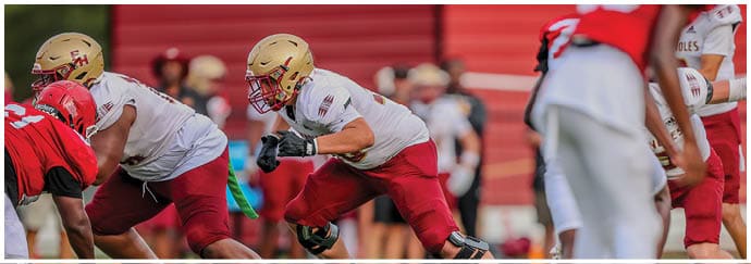 Several people wearing football uniforms are engaged in a play on a field with a red background. Description generated by AI