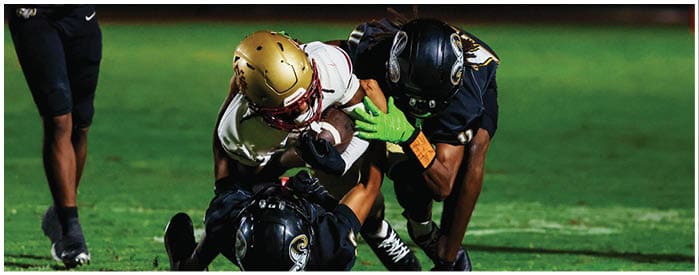 Two people in football gear are on a grassy field with one person tackling the other who is holding a football. Description generated by AI