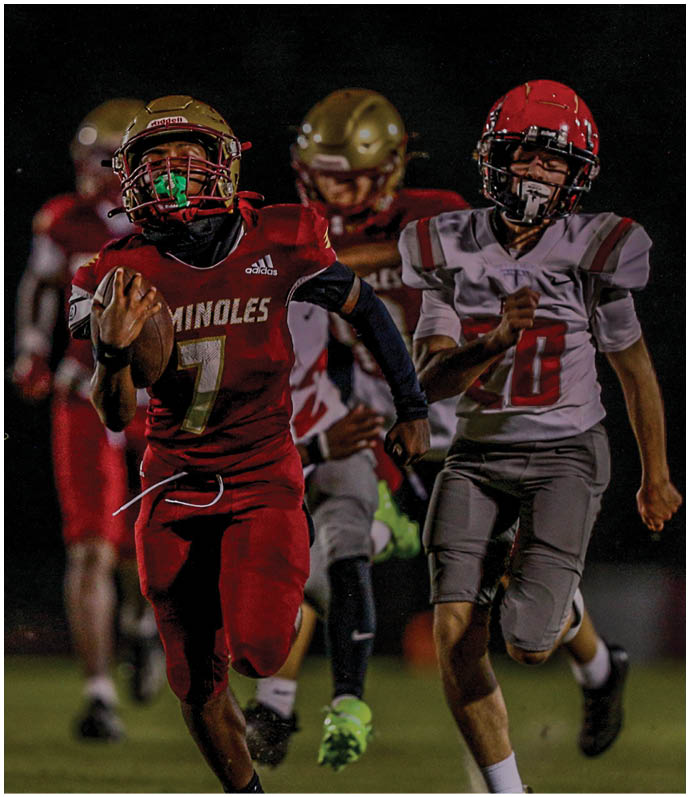 Several people in football uniforms are engaged in a close, intense tackle during a game on a grassy field. Description generated by AI
