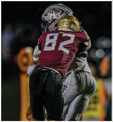 A person wearing a gold football helmet is visible at the bottom of the image against a dark background with partially visible illuminated numbers and letters on the left side. Description generated by AI