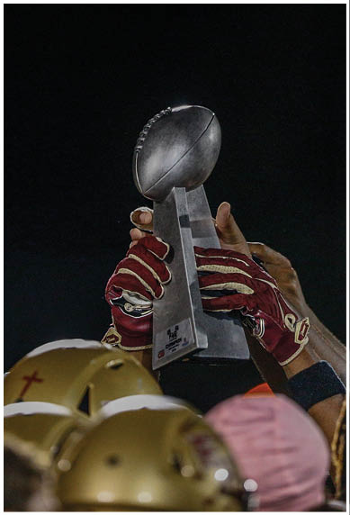 Two people wearing football uniforms and helmets are on a field at night with a bright light in the background. Description generated by AI