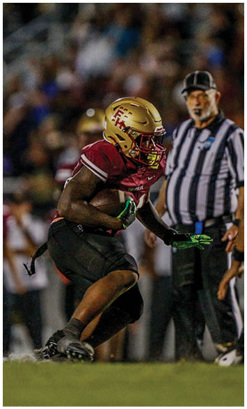 Two people wearing gold football helmets and white jerseys with “Seminoles" written on them are engaged in a conversation or huddle under bright lights. Description generated by AI