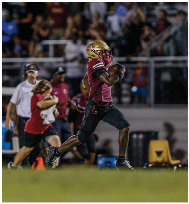 A person wearing a gold football helmet and uniform is seen behind several black helmets with a ram logo under bright stadium lights at night. Description generated by AI